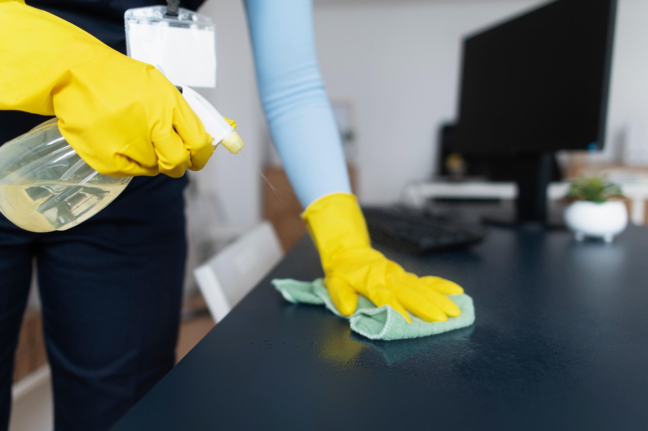 Gelbe Handschuhe reinigen einen Schreibtisch in einem Büro